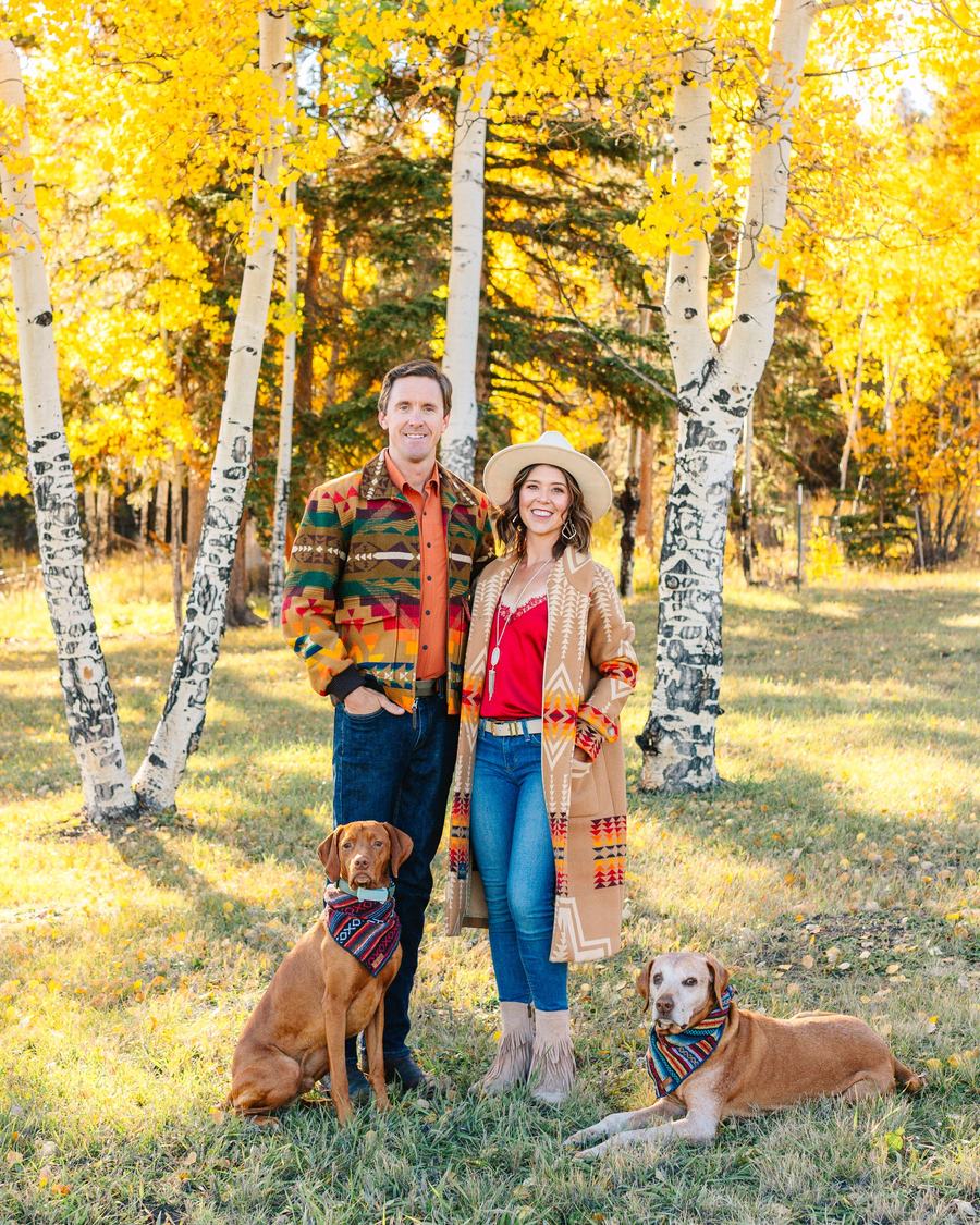 Danielle, her husband, and their two dogs in a grove of golden aspens, all in bold fall colors