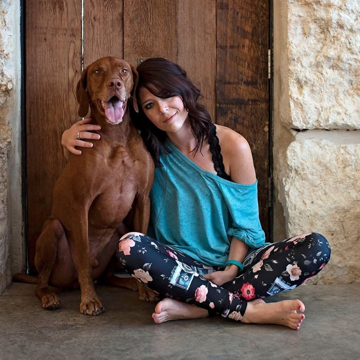 Danielle sitting cross-legged in front of a wooden door with Ruckus leaning in against her