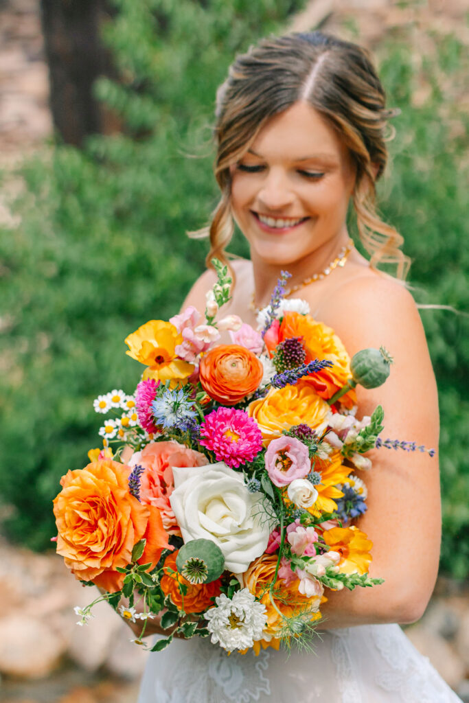 Bride smiling down at her colorful bouquet at Spruce Mountain Ranch