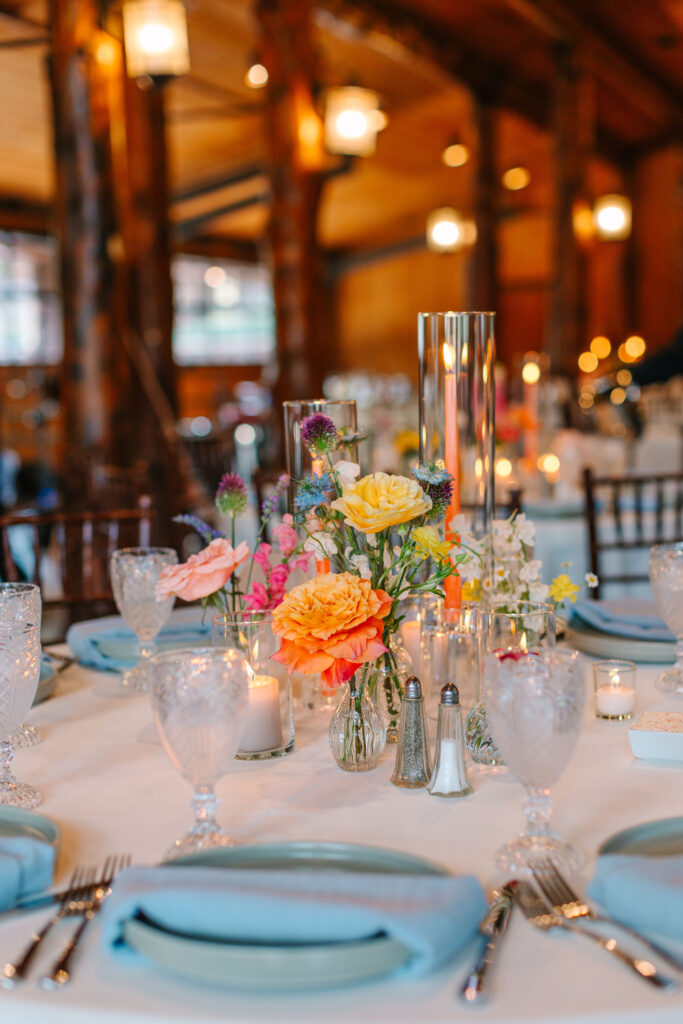 Table centerpiece with candles and vibrant summer flowers at the reception